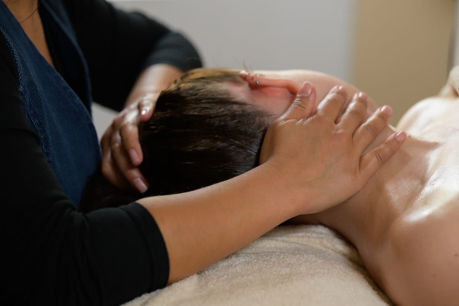 Massage du visage en institut, mains posées sur les tempes d'une cliente allongée